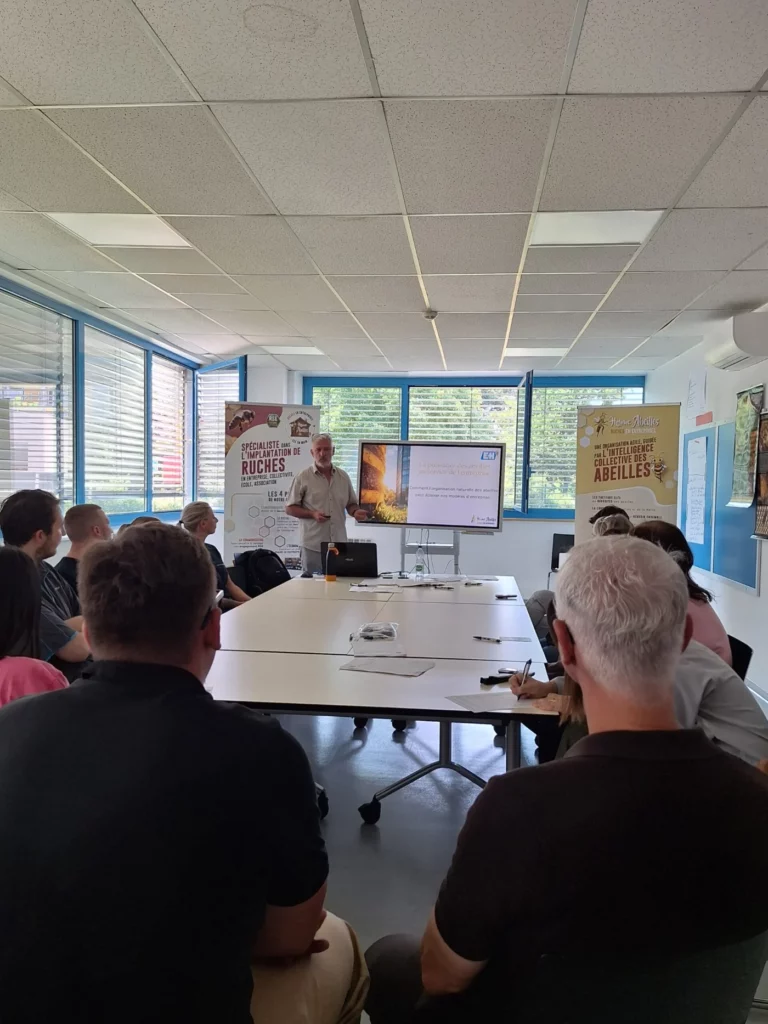 Participants d’une formation réunis autour de tables, Jean-Luc Jouhannet debout au fond de la salle
